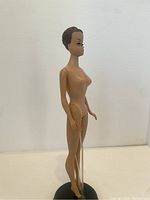 Side view of the nude Barbie doll showing slender figure, molded hair, and stand (stand not included).