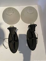 Two wall sconces with black metal bases and round frosted glass tops, placed side by side on a white background revealing size and details.