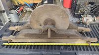 Top view of antique grinding stone wheel mounted on wooden frame with tape measure showing length around 30 inches.