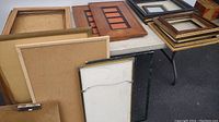 Photo showing assortment of picture frames laid out on a table, including backs and frames of various colors and finishes.