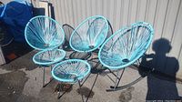 Set of five turquoise outdoor patio pieces including 2 rocking chairs, 2 round chairs, and 1 round side table on concrete surface against exterior metal wall. Shows weaving pattern and condition.