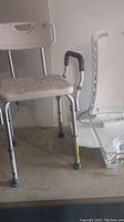 Adjustable shower chair and part of the lift seat frame seen on a table, showing metal legs with adjustable height.