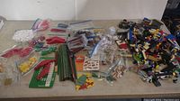 Wide view of entire lot showing various LEGO building pieces and bags of parts spread out on table.