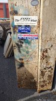Close-up of the rusted exterior side of the cabinet with old decals and stickers.