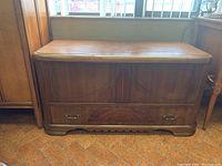 Front view of closed cedar chest showing hinged top, decorative veneer panels and brass handles.