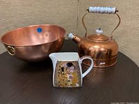 Photo showing copper mixing bowl, copper kettle with ceramic handle, and decorative creamer with artwork inspired by Gustav Klimt