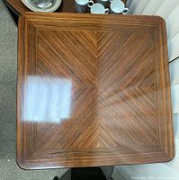 Close-up photo of one table top showing geometric wood veneer pattern with rich dark wood tone and glossy finish.