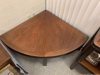 View of the pie slice-shaped coffee table corner with wood grain veneer top and dark legs, showing surface and shape.
