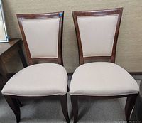 Front view of the two matching chairs showing beige upholstered seats and backs with dark wooden frames.