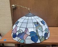 Clear photo of the stained glass hanging lamp on wooden table, lit chain and shade pattern visible