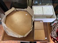 Large hexagonal gold metallic tile, smaller brown textured square tiles, and white tiles with green decorative design in a box