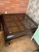 View of the coffee table showing dark wood frame with four glass panels forming the tabletop surface, legs curved outward.