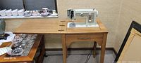 Sewing machine in wooden cabinet beside a table with glassware.