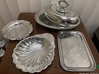 Photo showing all four items: the serving dish with cover, rectangular engraved tray, scallop shell plate, and round decorative plate