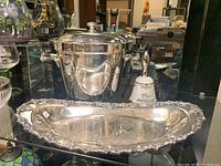 Overview of all three items together: silver plated oblong dish with grape motif, silver plated wine cooler with lid, and silver plated 25th anniversary bell.