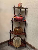 Full view of the four-tier corner shelf with turkey figurine on top, large red pumpkin with smaller pumpkin on second shelf, amber glass pumpkin on third, and clear glass pumpkin on bottom.
