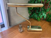 Side view of a polished brass vintage desk lamp with a cylindrical swivelling shade and rectangular weighted base.