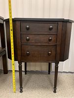 Side view of the vintage wooden sewing cabinet showing the three drawers and turned legs, with a measuring tape indicating height.