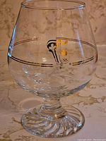 Single close-up photo of a Petro Canada Olympic brandy glass showing the gold-accented design and logo on the clear glass with swirled base.