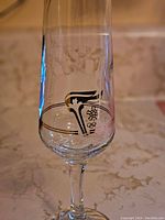 Close-up photo of a single champagne glass showing the etched and printed Olympic torch logo with Olympic rings and a snowflake symbol.