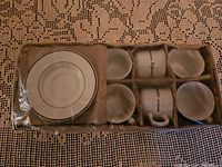 Top-down view showing six espresso cups and six saucers in a sectioned cardboard box with plastic wrap covering.
