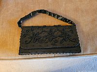 Black women's beaded evening purse with fabric handle, displayed on a light brown surface.