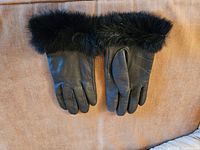 Pair of women's black leather gloves laid flat, showing faux fur trim around wrists on a tan surface