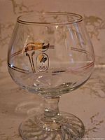Close-up photo of a single small brandy glass showing clear glass, short stem and Petro Canada Olympic logo with flame design in gold and black.