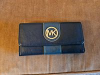 Front view of black leather Michael Kors wallet with gold MK logo on flap.