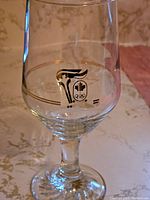 Close-up photo of one glass showing the gold and black torch design and Olympic rings logo beneath a maple leaf symbol in the center of the glass.
