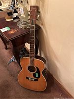 Full view of acoustic guitar leaning against wall next to table