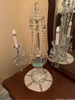 Electric crystal chandelier table lamp with three arms and hanging crystal prisms, placed on a wooden surface in front of a mirror.