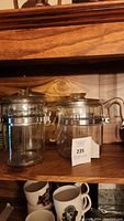 Two clear glass Pyrex percolator coffee pots side by side on wooden shelf