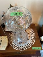 Top-down view of one crystal lamp showing detailed cut glass globe with floral and geometric patterns, placed on a wooden table with lace doily underneath.