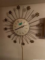 Full view of mid-century modern sunburst wall clock hanging on wall with metal spokes and flower accents