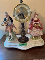 Front view of two porcelain musical statues and a clock set on marble base