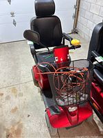 Front three-quarter view of red Fortress mobility scooter with black seat, basket on front, delta tiller and controls