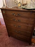 Front view of tall boy chest showing the five wood veneer drawers and metal handles with decorative accents.