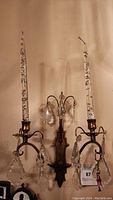Full front view of vintage French wall sconce showing two arms supporting candles with tall decorative glass covers and hanging crystal prisms.