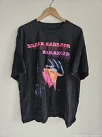 Black short-sleeve T-shirt with large graphic and text print on front referencing Black Sabbath's Paranoid album.