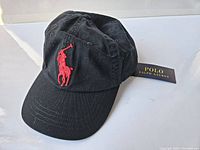 Front view of black baseball cap with large red embroidered polo player logo and Polo Ralph Lauren tag attached.