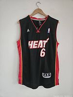 Black Miami Heat LeBron James basketball jersey with number 6 front view hung on a wooden hanger.