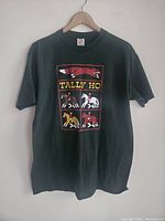 Front full view of black vintage Tally Ho T-shirt hanging on wooden hanger