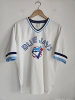Front view of white vintage Blue Jays baseball jersey hanging on hanger showing front logo and text