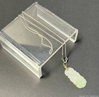 Necklace chain and jade Buddha pendant displayed on a clear plastic stand showing full length and detail.