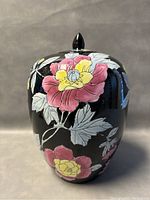 Front view of the ginger jar showing pink and yellow flowers against black background with the lid on top.