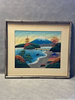 Framed watercolor painting of a Japanese landscape depicting Mount Fuji, pagodas, trees and water, with beige matting and silver bamboo frame.