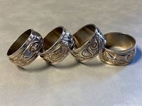 Four pewter napkin rings with First Nations style engravings lying on grey surface, showing side views of detailed designs.
