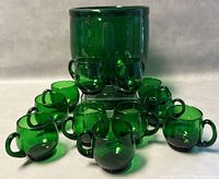 Front view of footed green glass punch bowl surrounded by twelve matching cups.