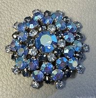 Front view of the round Lugano crystal brooch showing blue and clear faceted crystals arranged in a floral pattern.